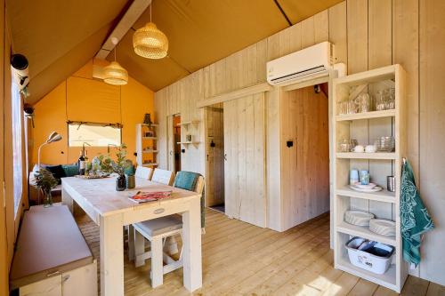 a room with a table and a kitchen with yellow walls at Camping Vossenberg - op de Veluwe! in Epe