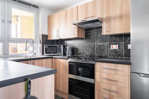 een keuken met houten kasten en een zwarte kookplaat bij Lovely 1-bedroom property with balcony in West end in Glasgow