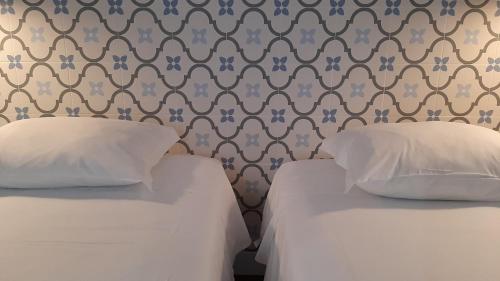 two beds with white pillows in a room with wallpaper at A Casa do Tenente in Faro
