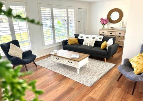 a living room with a black couch and two chairs at 47 Murrah - Lux 3 bed home, walk to everything - Pet friendly in Bermagui