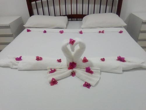 Una cama con sábanas blancas y flores rosas. en Apartamento com 2 quartos no centro de Pipa, en Pipa