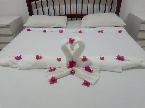 a bed with white sheets and pink flowers on it at Apartamento com 2 quartos no centro de Pipa in Pipa