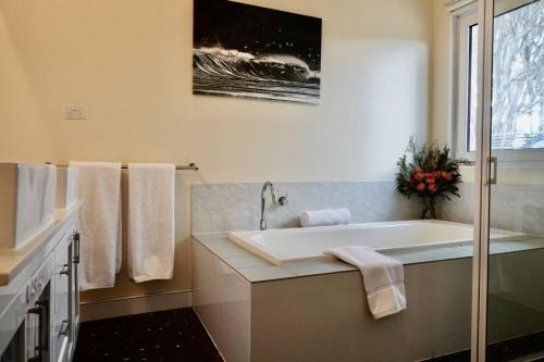 La salle de bains blanche est pourvue d'une baignoire et d'une fenêtre. dans l'établissement Waterfront 'Jemadda' Family Lodge, à Bream Creek