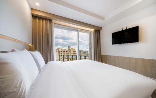 a bedroom with a white bed and a large window at Geoje Mongdol Beach H Avenue Hotel in Geoje 