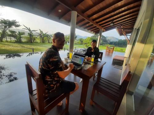 a man sitting at a table with a laptop at MARGOSA MOUNTAIN VILLA in Galewela