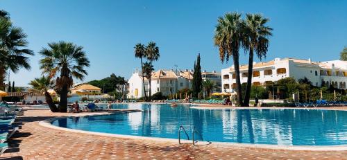 une grande piscine avec des palmiers et des bâtiments dans l'établissement Cabanas Acqua Golden, à Cabanas de Tavira