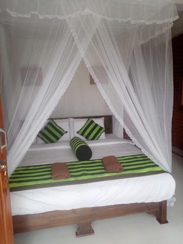 a bed with green and white pillows and a canopy at adam's apple homestay in Ella