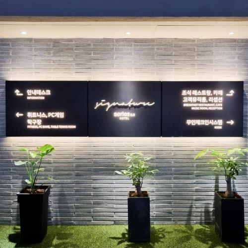 two potted plants in front of a wall with signs at Daegu Seongseo Hotel Series 5.0 in Daegu