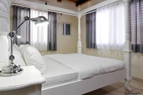 a white bedroom with a bed and a lamp on a table at Villa Troya in Safed