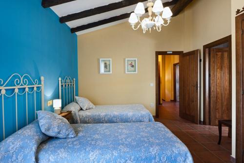 two beds in a bedroom with blue walls and a chandelier at Casa Rural El Caldero in Sorihuela