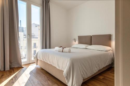 a white bedroom with a large bed and a large window at WeLive Trapani - luxury apartments in Trapani