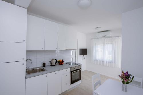 uma cozinha com armários brancos, um lavatório e uma mesa em Apartments Una em Poljica