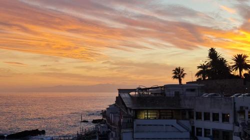 zachód słońca nad oceanem z palmami na szczycie budynku w obiekcie Enjoy Home w Genui