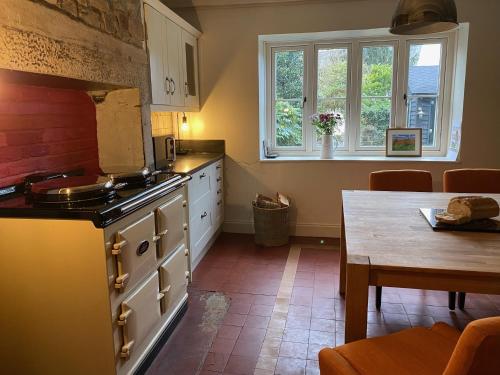 a kitchen with a stove and a table in it at 4 bedroom coastal cottage with walled garden in Embleton