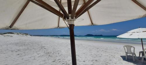 una playa con 2 sillas y una sombrilla en la arena en Suite simple perto praia, en Cabo Frío