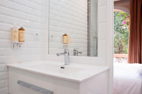 La salle de bains blanche est pourvue d'un lavabo et d'un miroir. dans l'établissement Hôtel Le Porquerollais, à Porquerolles