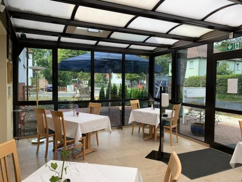 un restaurante con mesas y sillas blancas y ventanas en Hotel Blaufuchs en Petershagen