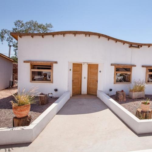 a white house with wooden doors and windows at Hotel La Cochera in San Pedro de Atacama