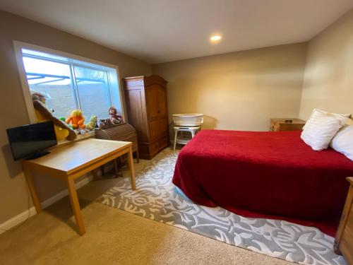 een slaapkamer met een rood bed, een bureau en een raam bij Private basement bedroom with private bathroom, kitchen, and living room with large screen television in McCordsville