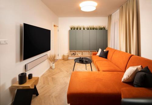 a living room with an orange couch and a flat screen tv at Hillside Kubínska Hoľa - Apartmán Bird's eye view in Dolný Kubín