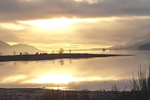 una puesta de sol sobre un cuerpo de agua con montañas en el fondo en Fort William loft on shore front with amazing views en Caol