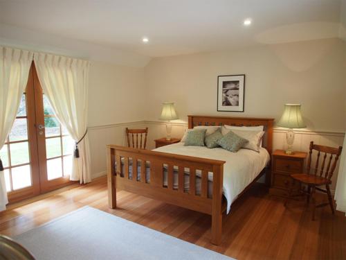 a bedroom with a bed with two chairs and a window at Tahara Cottage in Deloraine