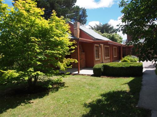 a small red house with a grass yard at Tahara Cottage in Deloraine