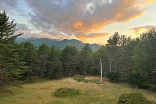 a field with trees and a sunset in the background at Adirondack Mountain View Retreat in Elizabethtown