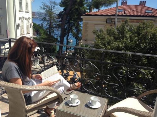a woman sitting in a chair reading a book on a balcony at Luxury Apartments Centre of Opatija in Opatija