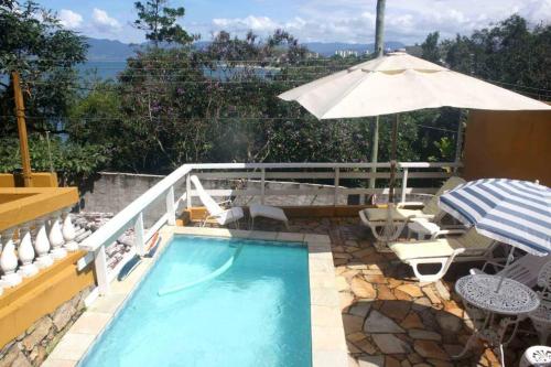 una piscina con sombrilla, mesa y sillas en Por de sol no mar da cama, en Caraguatatuba