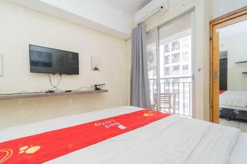 a bedroom with a bed with a tv and a window at RedLiving Apartemen Serpong Green View - Farida Property in Ciater-hilir