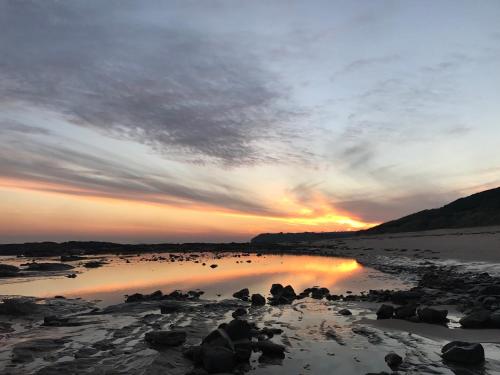 a sunset on a beach with rocks in the water at Ocean & Country Views, Spa, Pets Welcome, Fireplace - Your Ocean Oasis 10 minutes to Phillip Island in Kilcunda