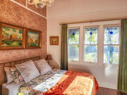 ein Schlafzimmer mit einem Bett und zwei Fenstern in der Unterkunft Elroma, a grand Federation house in Hepburn Springs in Hepburn Springs