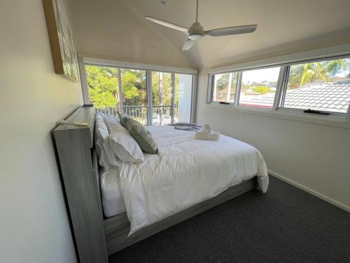 a bedroom with a bed with white sheets and windows at Noahs Beach House - at Flynns in Port Macquarie