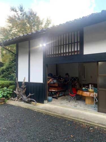 a house with a man sitting at a table in front of it at 佐渡島に残る築130年の伝統的な古民家｜東夢 in Sado
