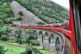 a red train traveling over a bridge with a mountain at Mortirolo in Mazzo di Valtellina