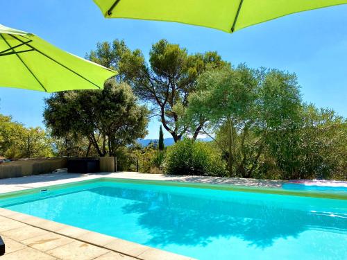a swimming pool with a green umbrella and trees at Mas d'Olea in Lauris
