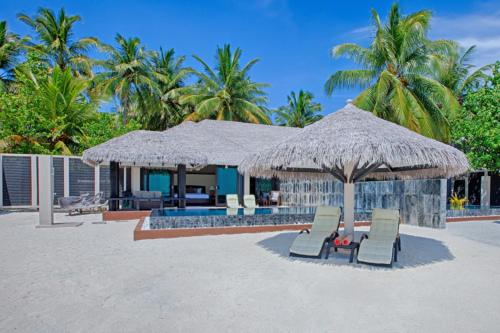 Villa con sombrilla de paja y sillas en la playa en Kihaa Maldives, en Atolón Baa
