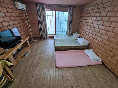 a room with two beds and a tv and a brick wall at Joy Red Clay Resort in Jeju