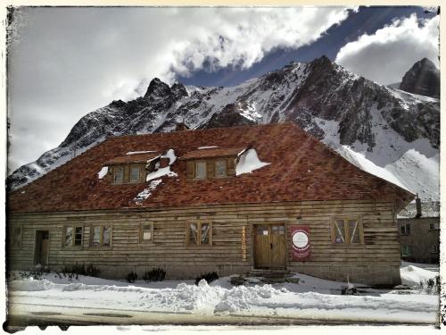 a wooden house in front of a snow covered mountain at Portezuelo del Viento - Hostel de Montaña in Las Cuevas