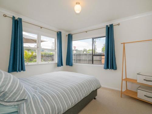 a bedroom with blue curtains and a bed and two windows at Beach House on Hetherington - Whangamata Home in Whangamata