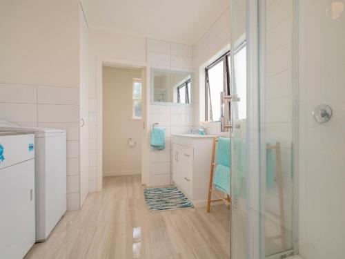 a white bathroom with a sink and a shower at Beach House on Hetherington - Whangamata Home in Whangamata