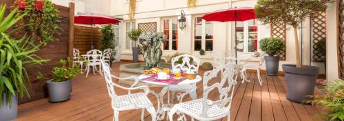 un patio con sillas y mesas blancas y sombrillas rojas en Agate Hôtel en París