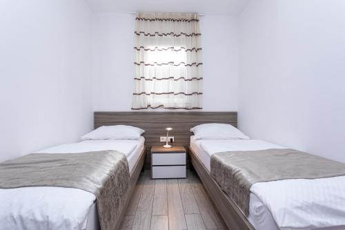 a bedroom with two beds and a table with a window at Apartments Crnekovic Tomislava 8 in Baška