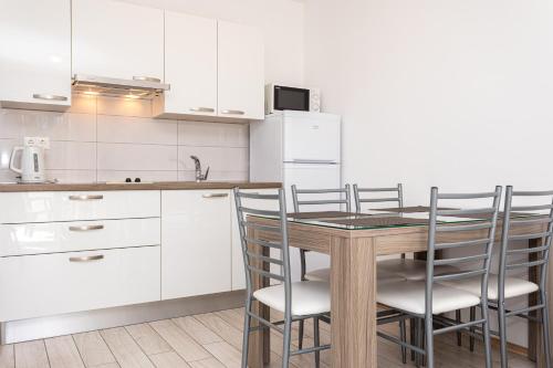a kitchen with white cabinets and a wooden table and chairs at Apartments Crnekovic Tomislava 8 in Baška