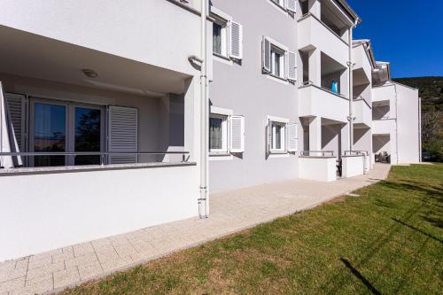 a white apartment building with a green lawn at Apartments Crnekovic Tomislava 8 in Baška