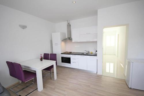 a white kitchen with a white table and purple chairs at Apartmani Sea Star in Makarska