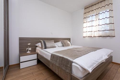 a white bedroom with a large bed and a window at Apartments Crnekovic Tomislava 8 in Baška