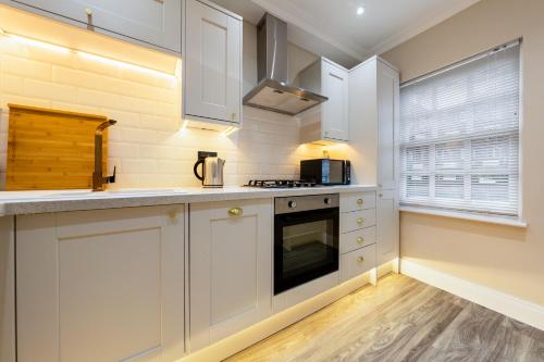 a kitchen with white cabinets and a stove at Canary Wharf Beautiful Modern House in London