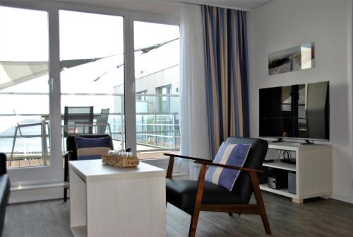 salon z telewizorem, biurkiem i krzesłami w obiekcie Apartmenthaus Hafenspitze Ap 42 "Segler", mit Sauna, Blickrichtung offene See - a72332 w mieście Eckernförde